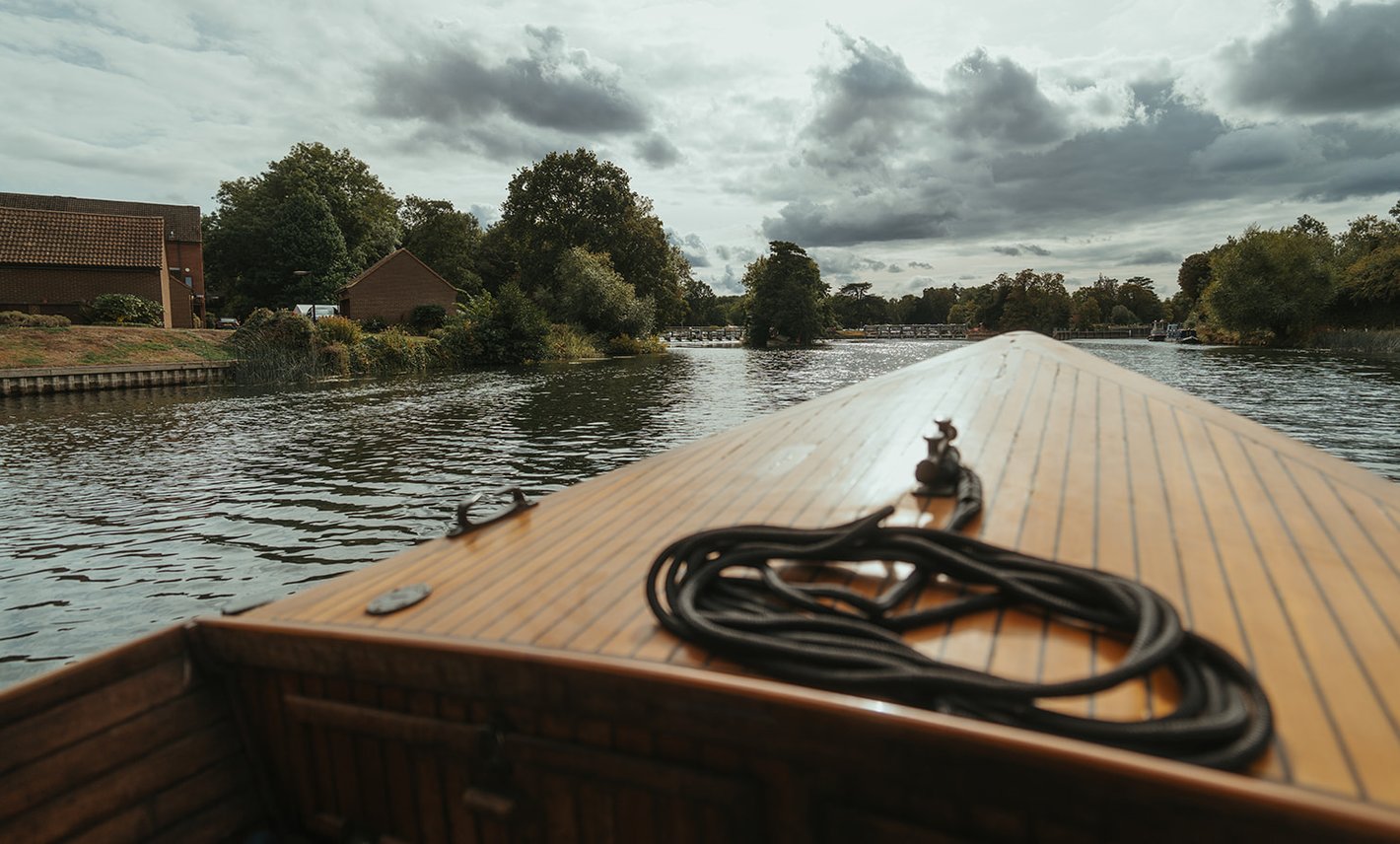 The teak bow of Queen of the Slipstream cruising the River Thames under a dramatic sky