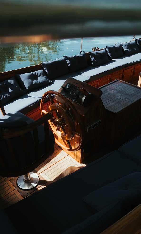 The helm, captain's chair and cushioned seating aboard, beside the river