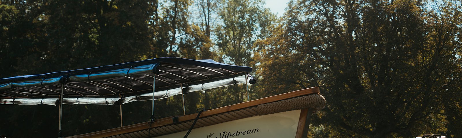 Queen of the Slipstream moored on a sunlit, tree-lined bank of the River Thames