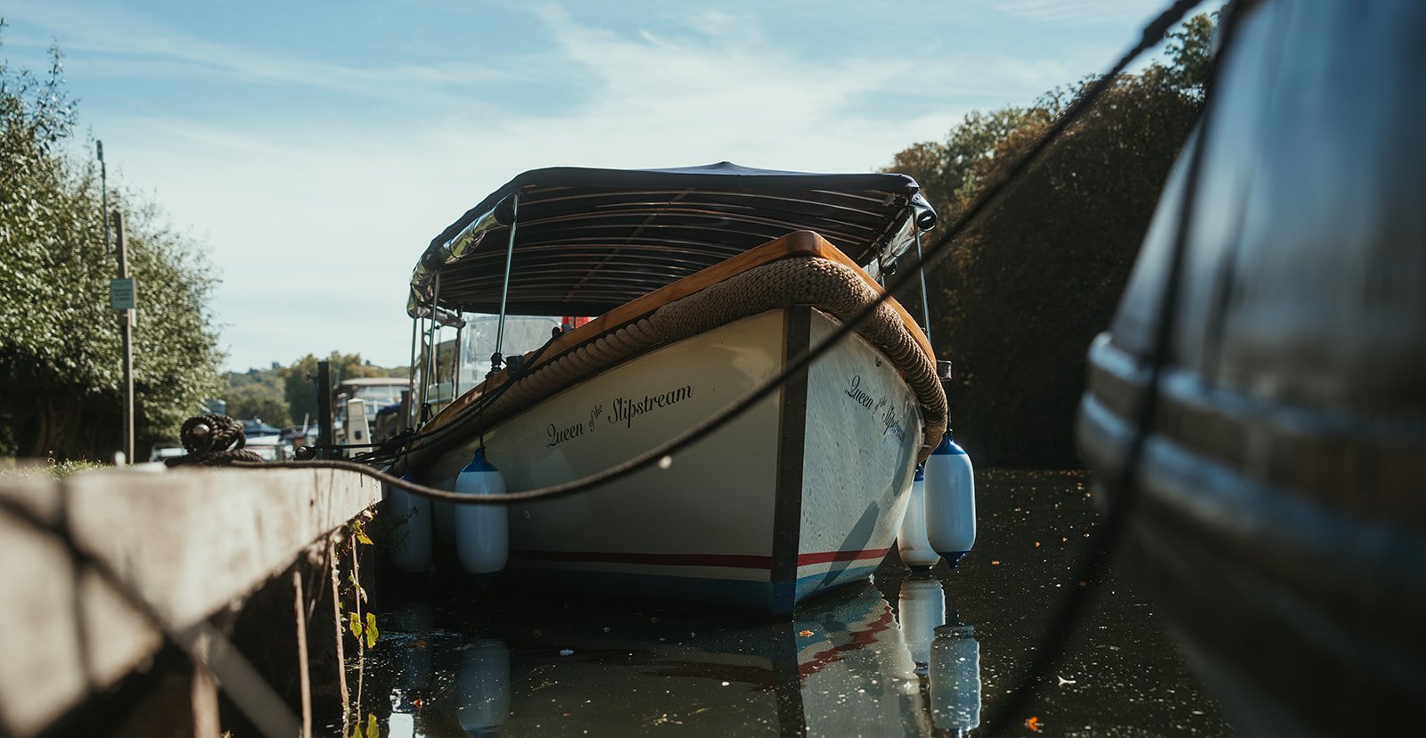Queen of the Slipstream, a traditional Thames launch, moored on a sunny day with her reflection in the river