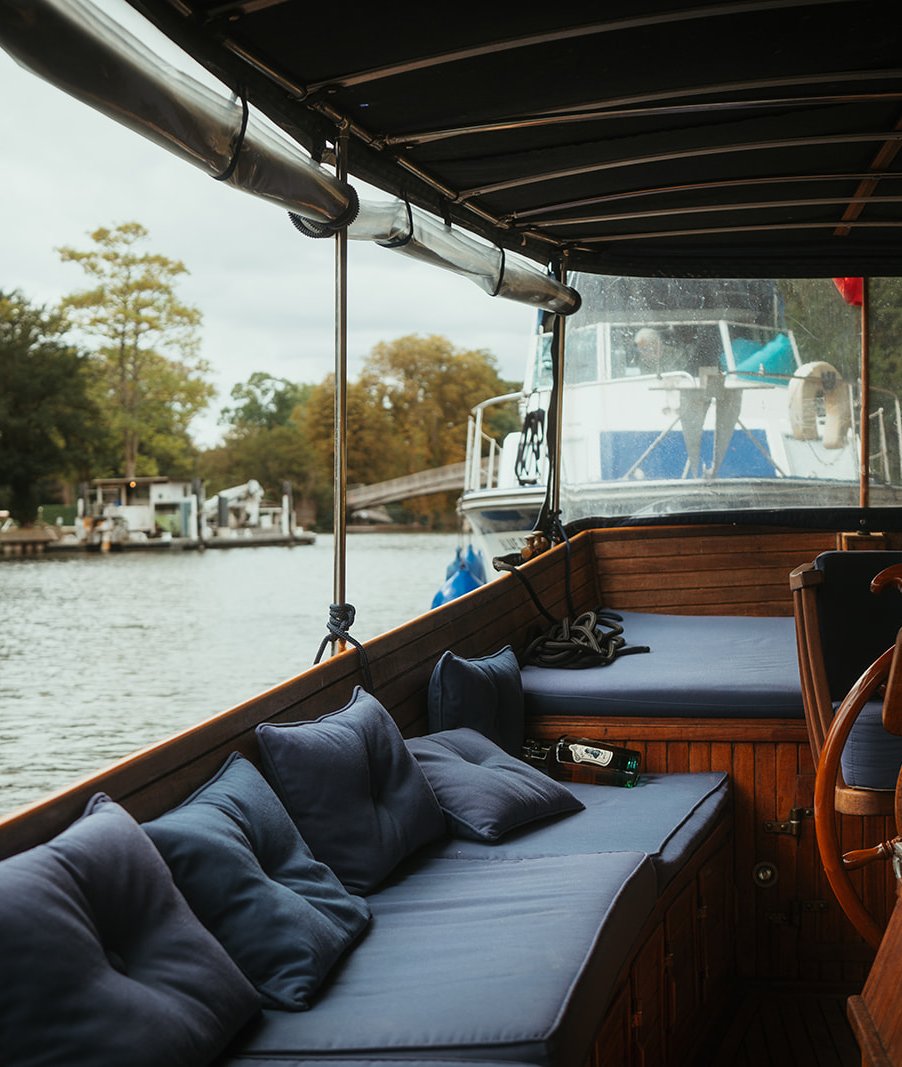 Cushioned seating and the helm aboard, cruising past moored boats on the Thames