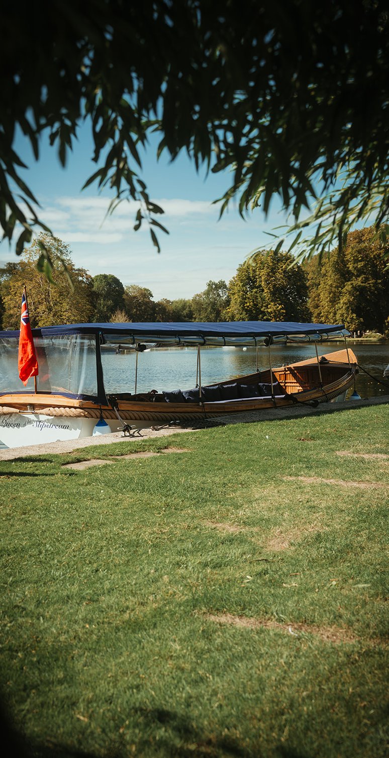 Queen of the Slipstream with her red ensign, moored on a riverside lawn beneath willow branches